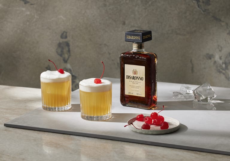 Disaronno Sour med en flaska Disaronno i bakgrunden