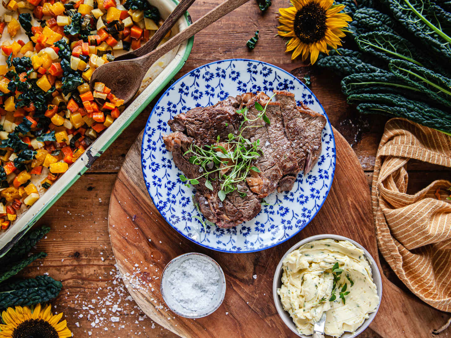 Entrecôte på vitblå tallrik, tärnade rotfrukter i panna och vispar kryddsmöt i vit skål.