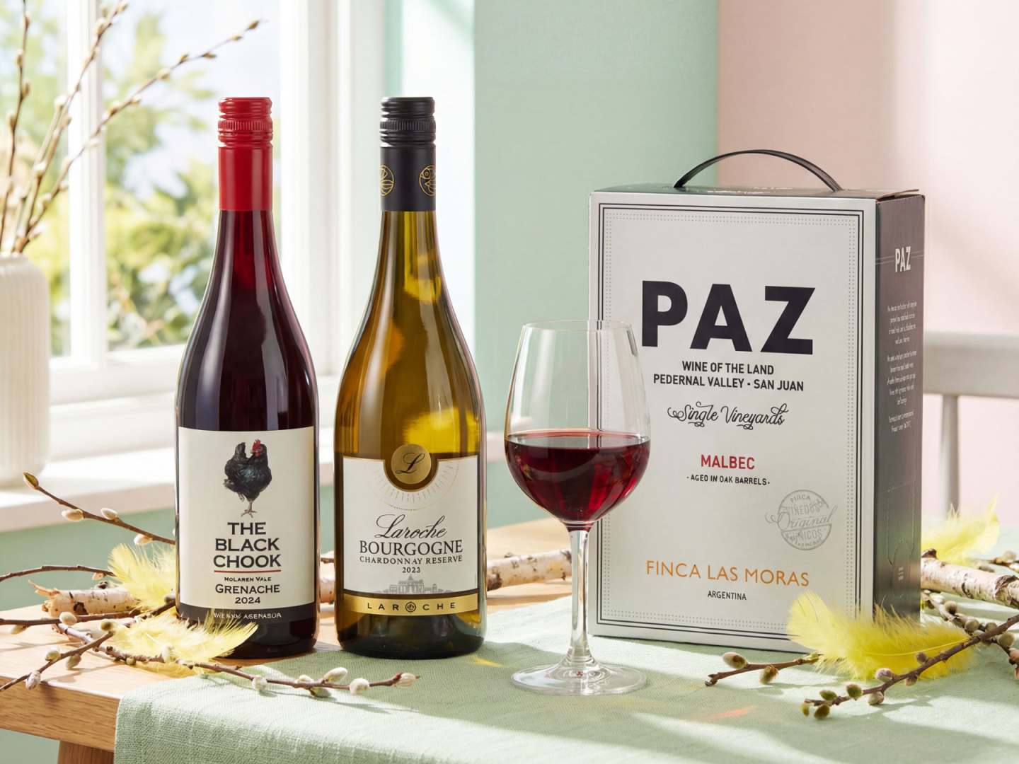 Tre viner på ett bord med påskris och fjädrar.