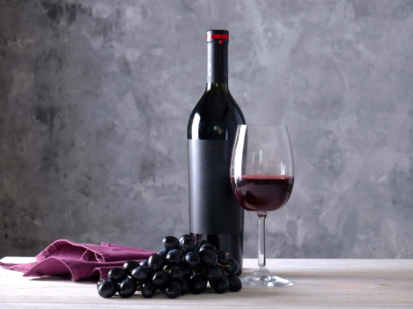 Cabernet Sauvignon på flaska, i vinglas och sin druvklase med grå bakgrund.