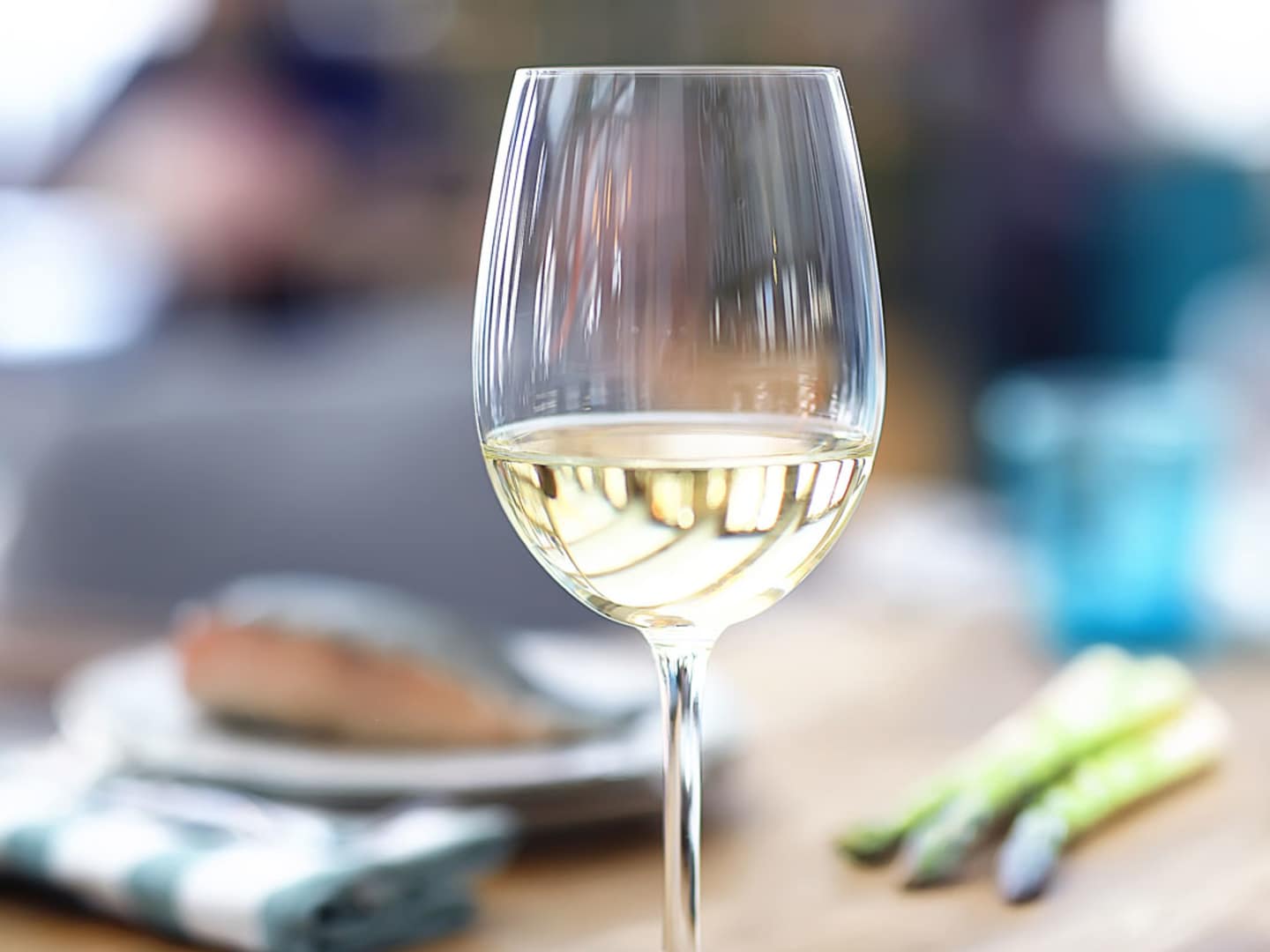 Rieslingvin i ett glas med fiska och sparris i bakgunden.