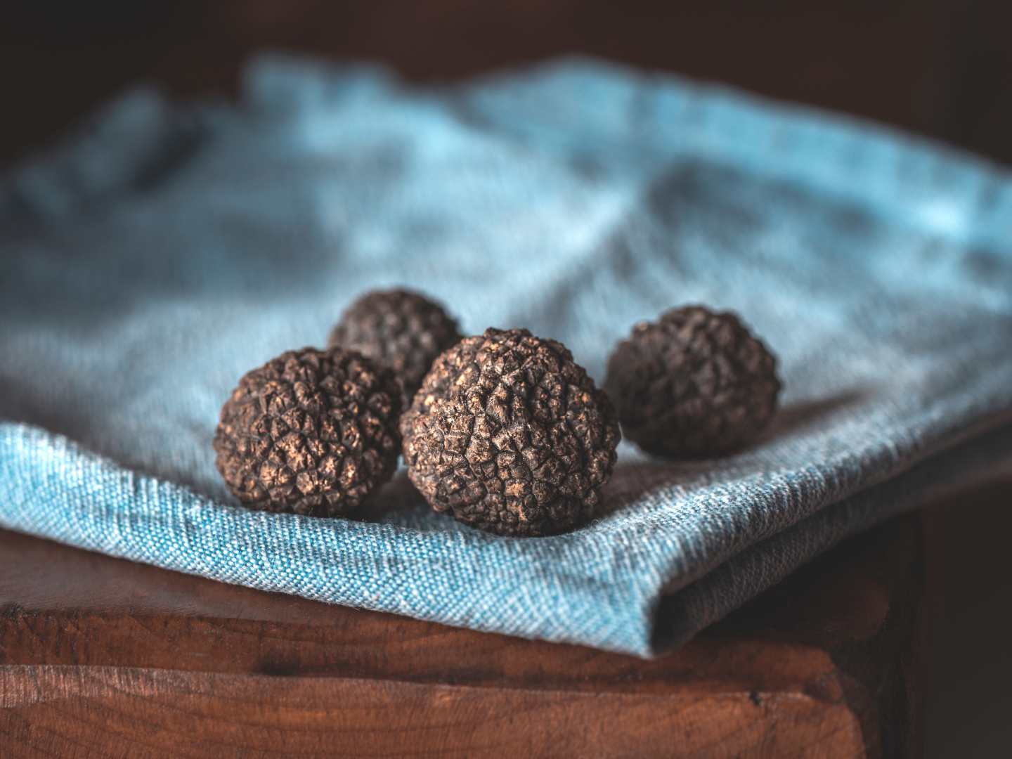 Fyra svarta tryfflar på en blå duk på ett träbord.