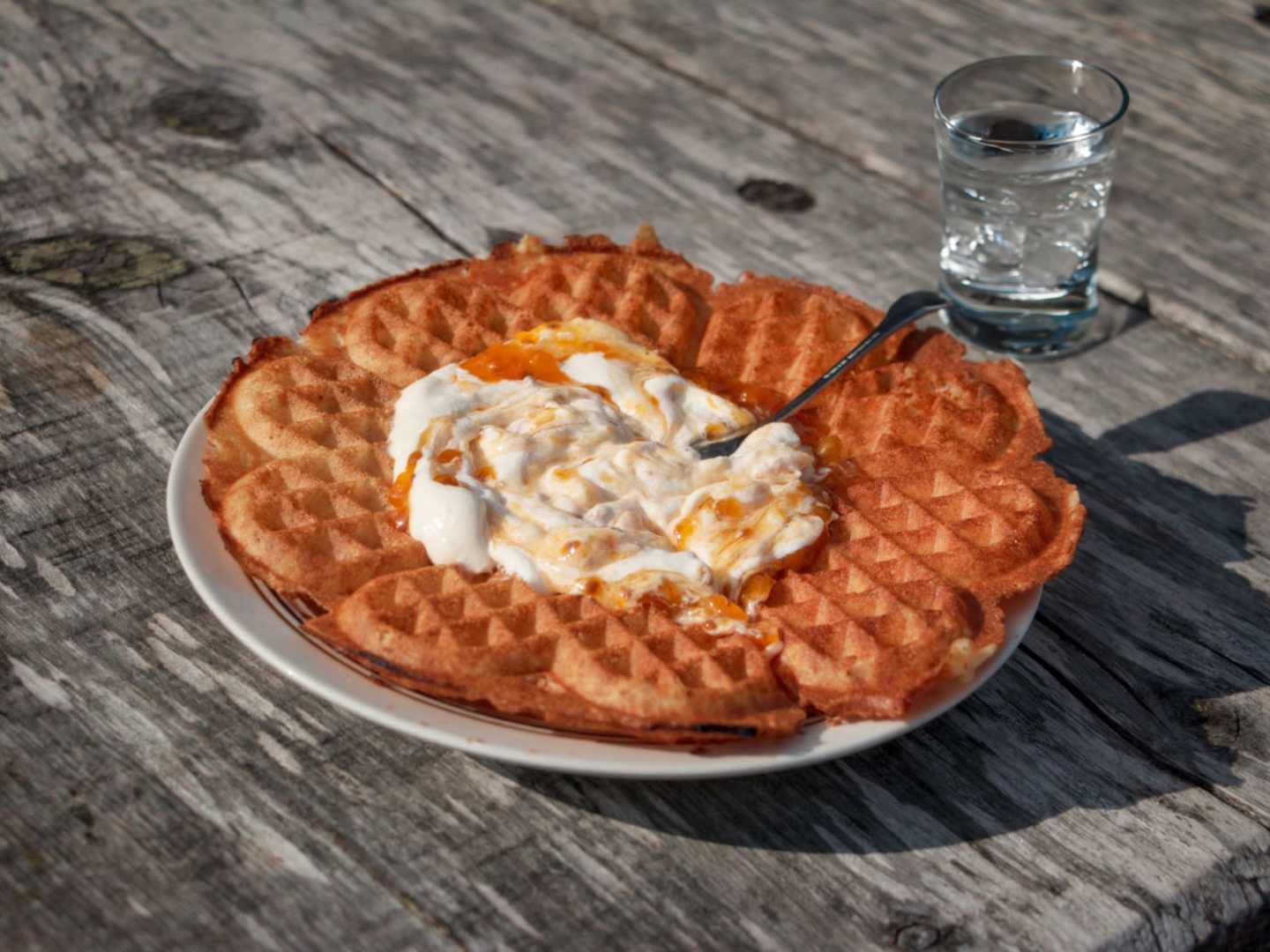 Våffla med hjortronsylt och grädde, och ett glas bubbelvatten bakom.