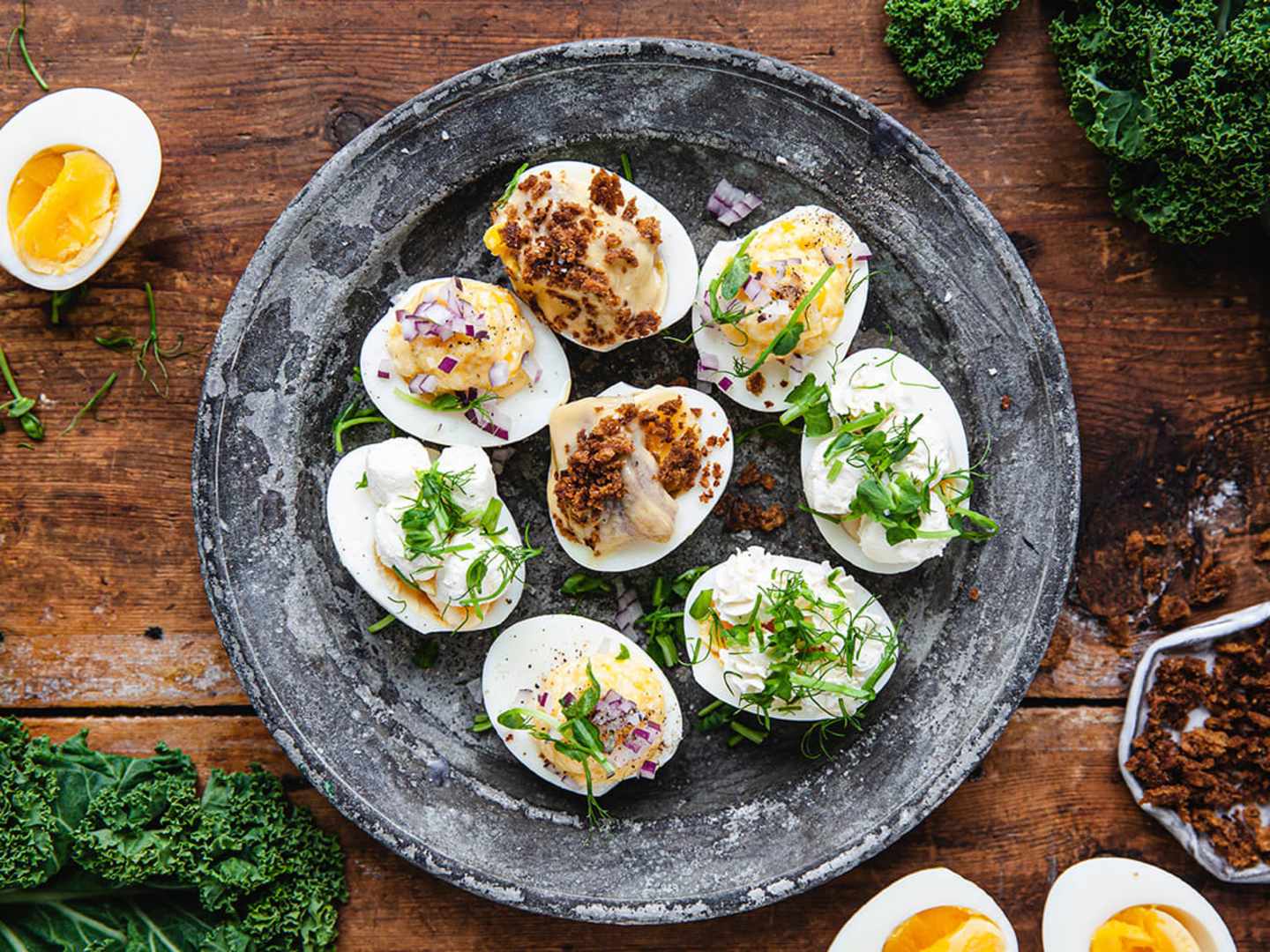 Ägghalvor med tre olika fyllningar på en tallrik på ett träbord.