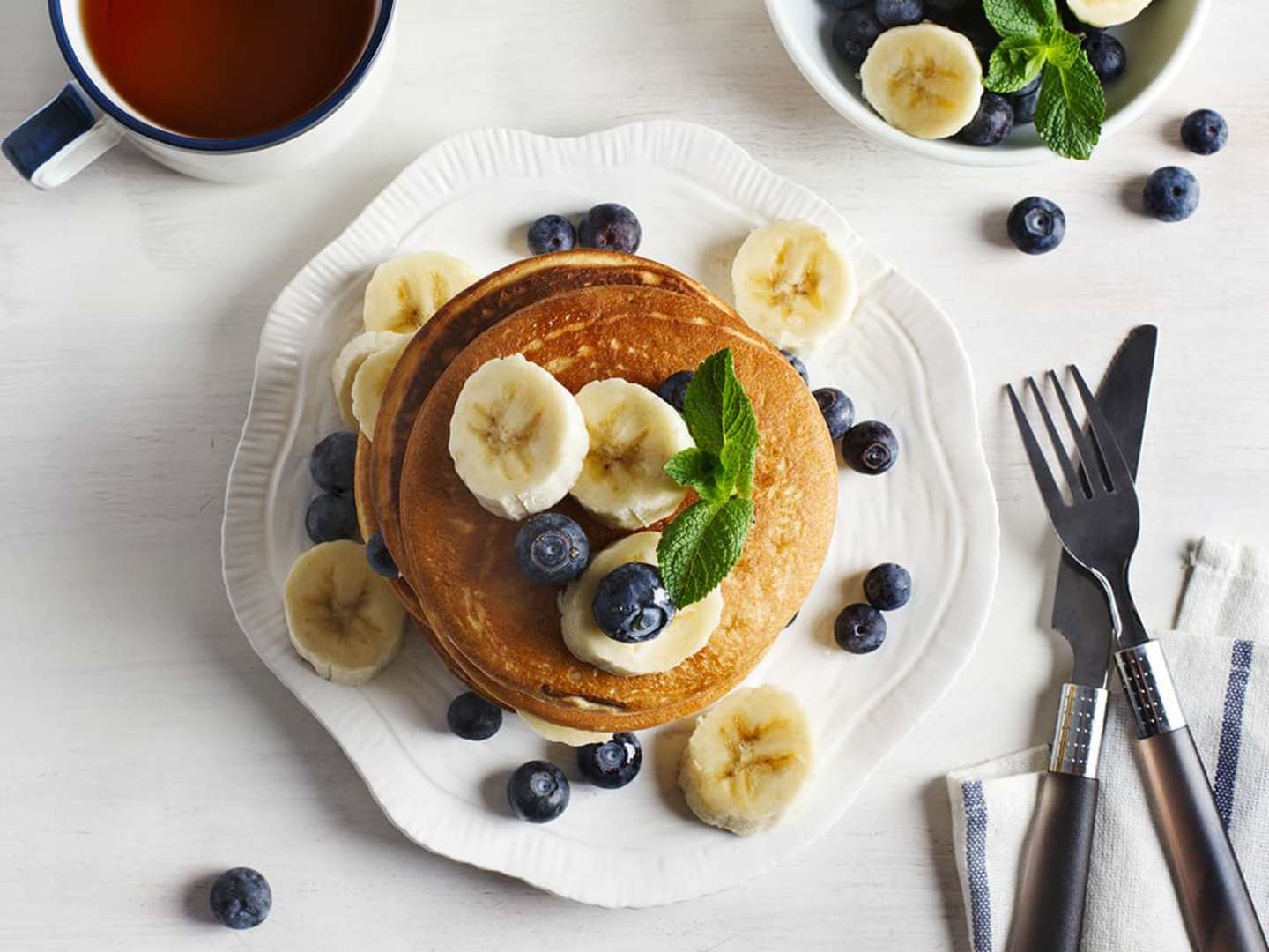 Veganska bananpannkakor med bananskivor och blåbär på vit tallrik.
