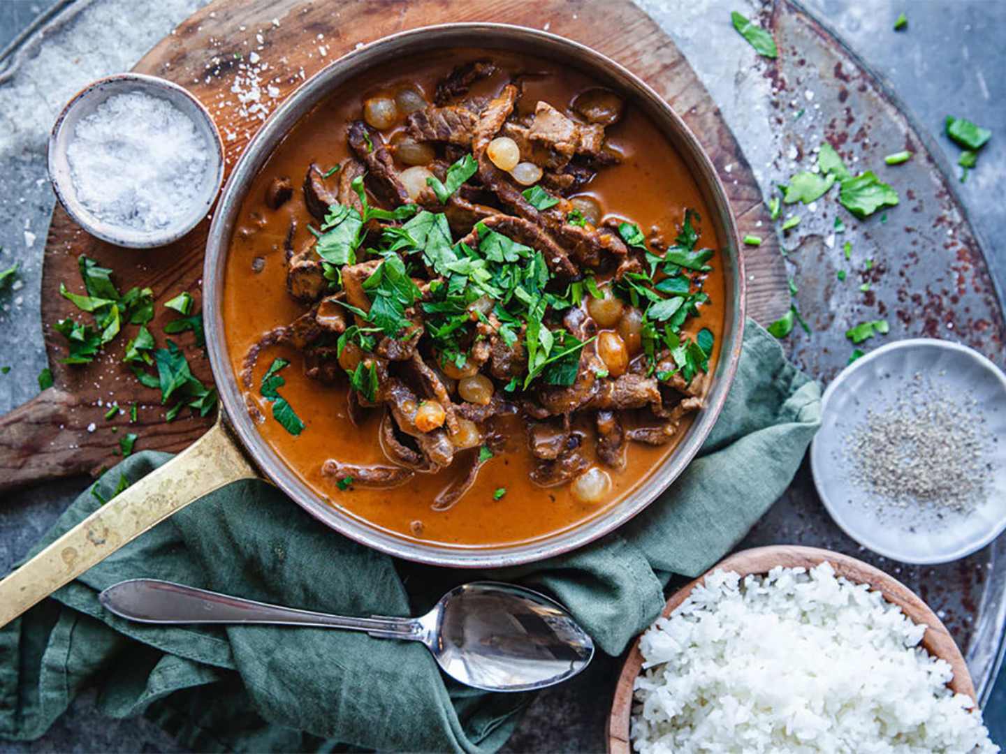 Lövbiffsgryta i stekpanna på bord med ris och salt.