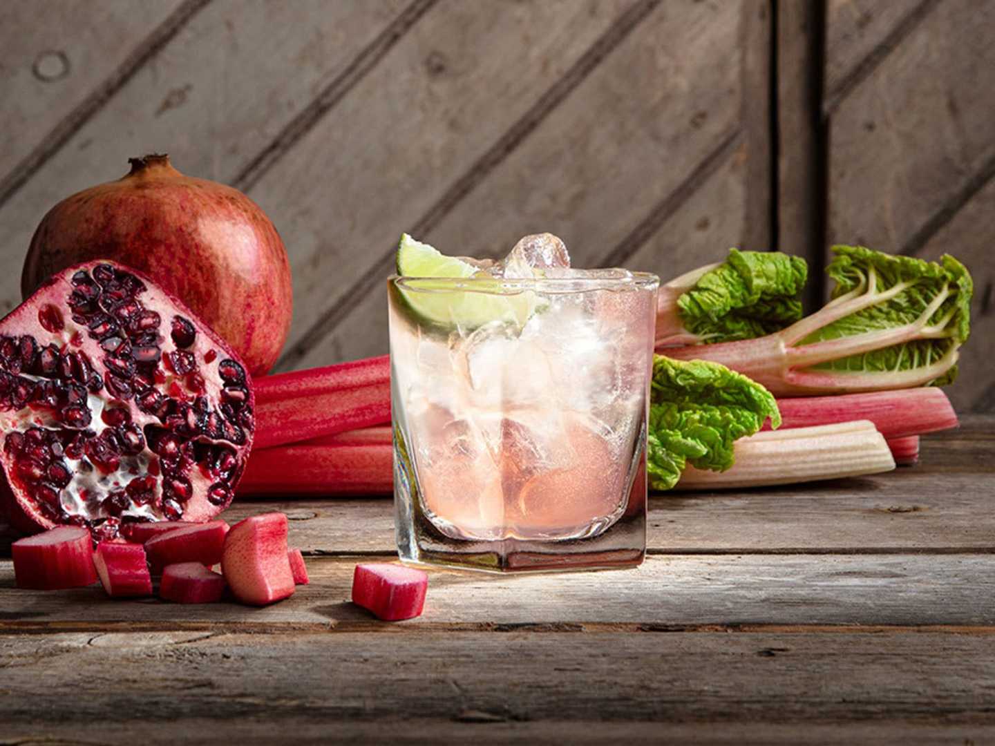 Ett rosa cocktailglas med rabarber och granatäpple bredvid 