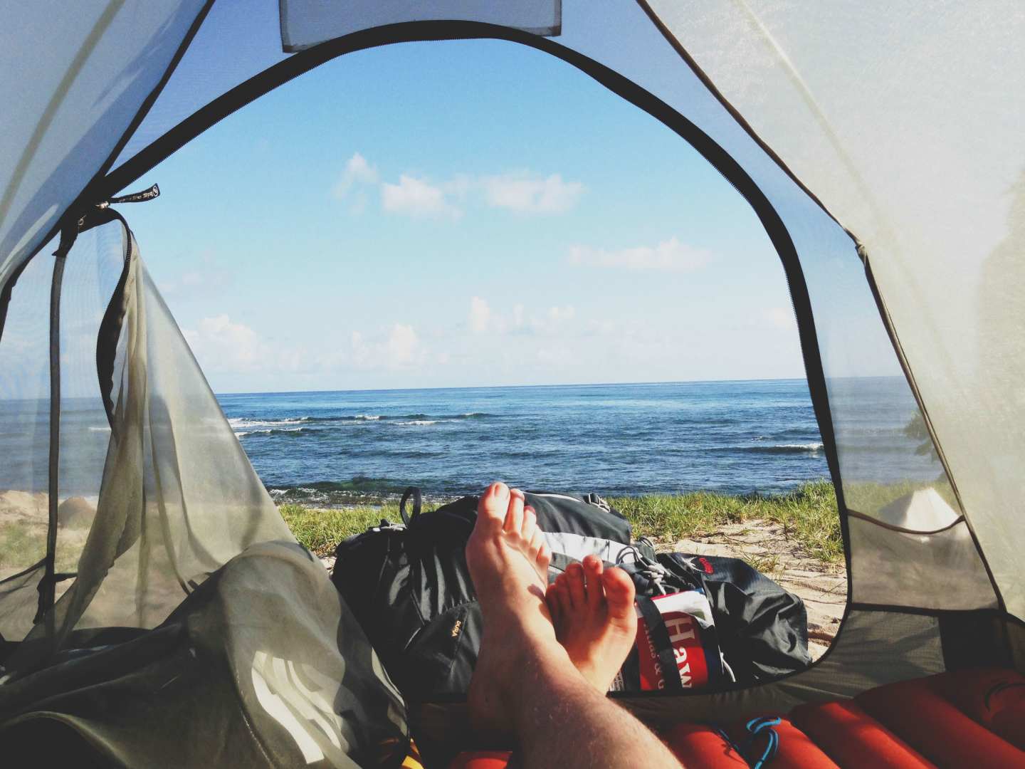 Bild på fötter utanför ett tält vid vattnet