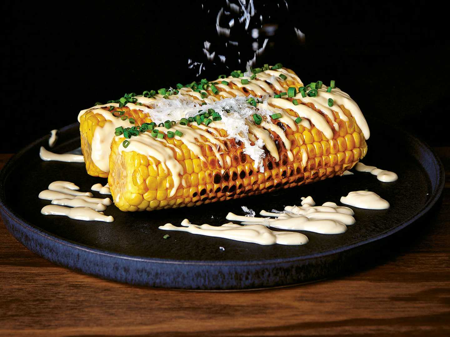 två grillade majskolvar på svart fat 