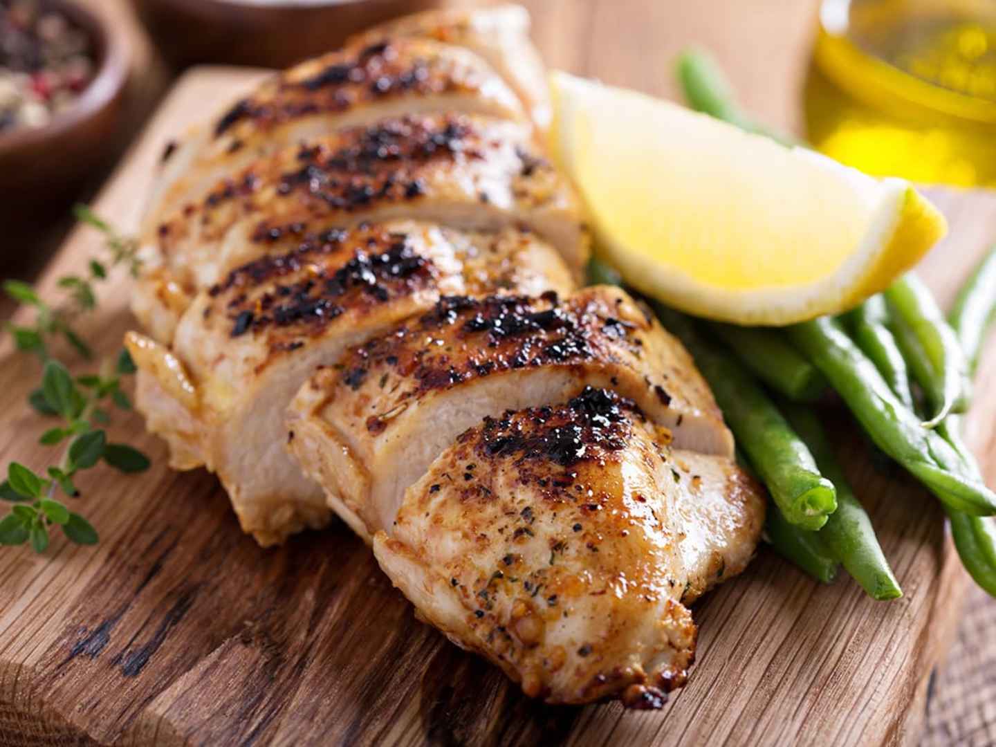 Kyckling i ugn med vitlök, citron och timjan, på skärbräda med haricots verts och en citronklyfta.