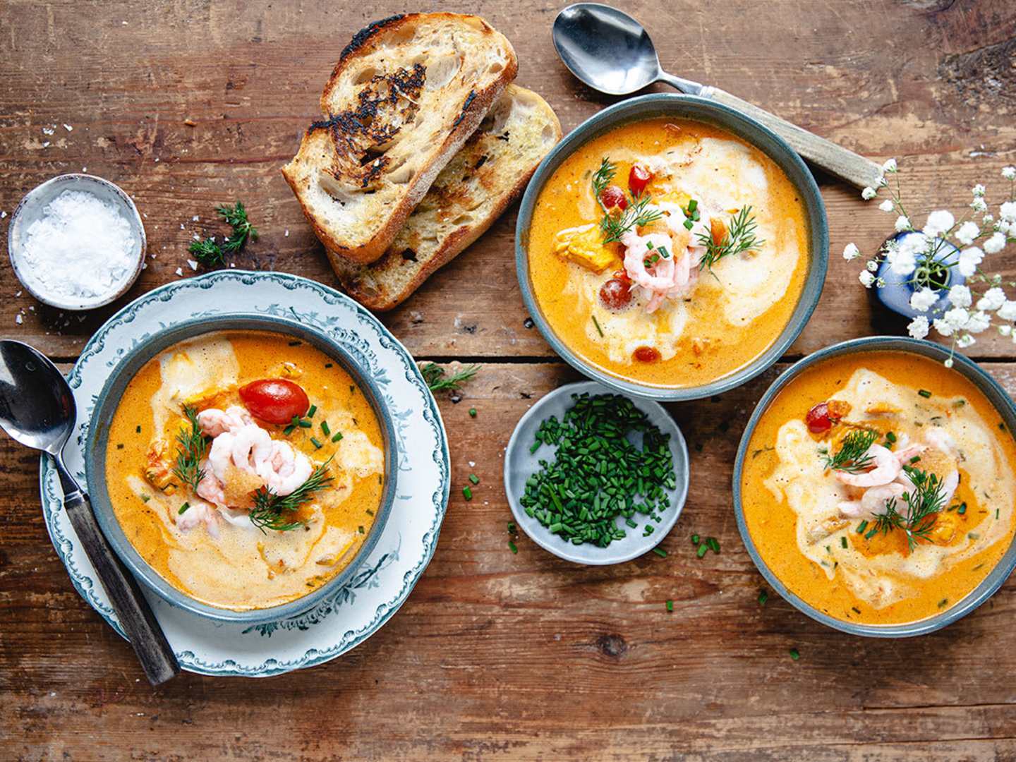 Ett träbord med tre skålar med gul soppa och vitlöksbröd. 