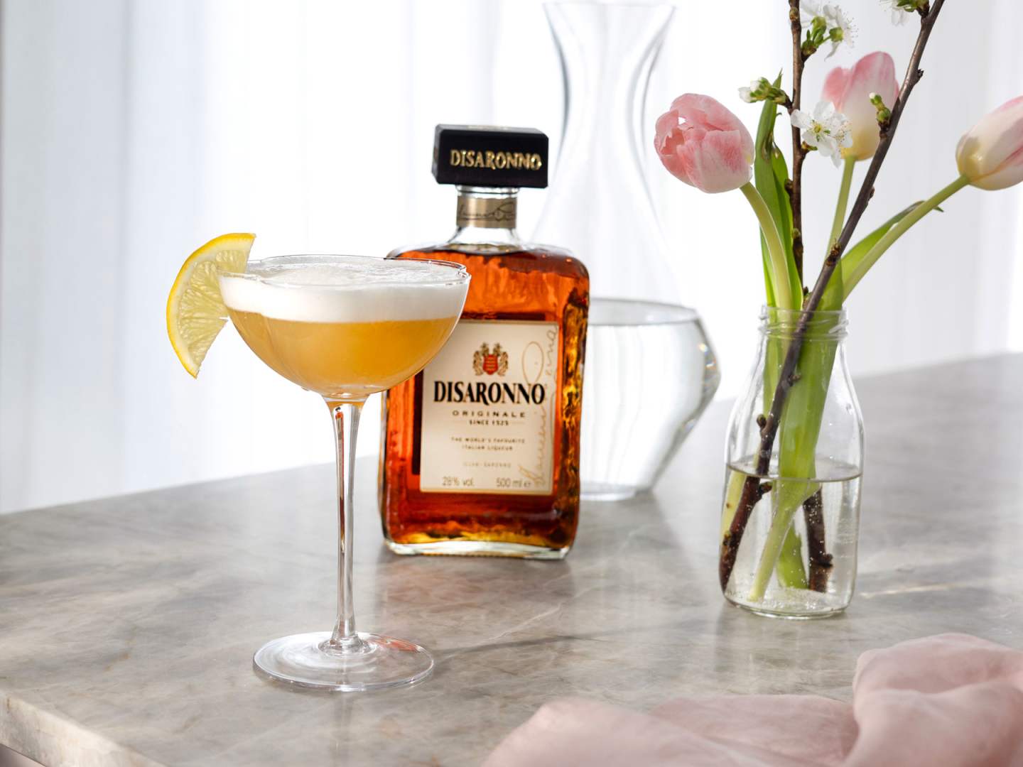 Disaronno Sour med en flaska Disaronno i bakgrunden