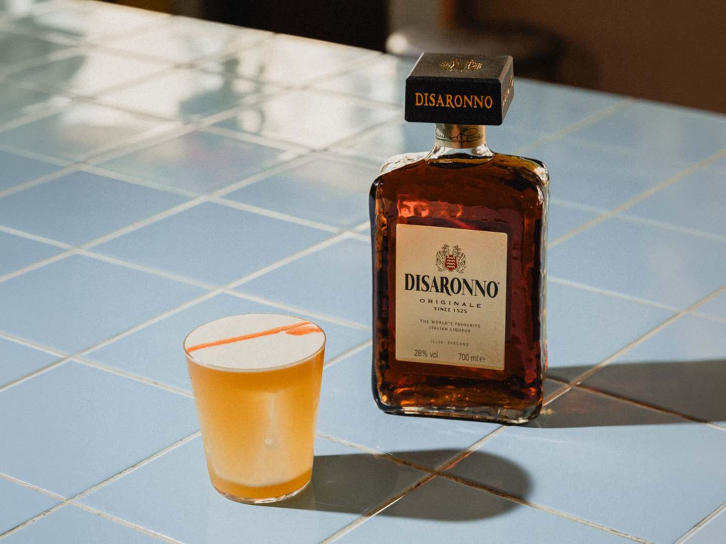 Disaronno Sour med en flaska Disaronno i bakgrunden