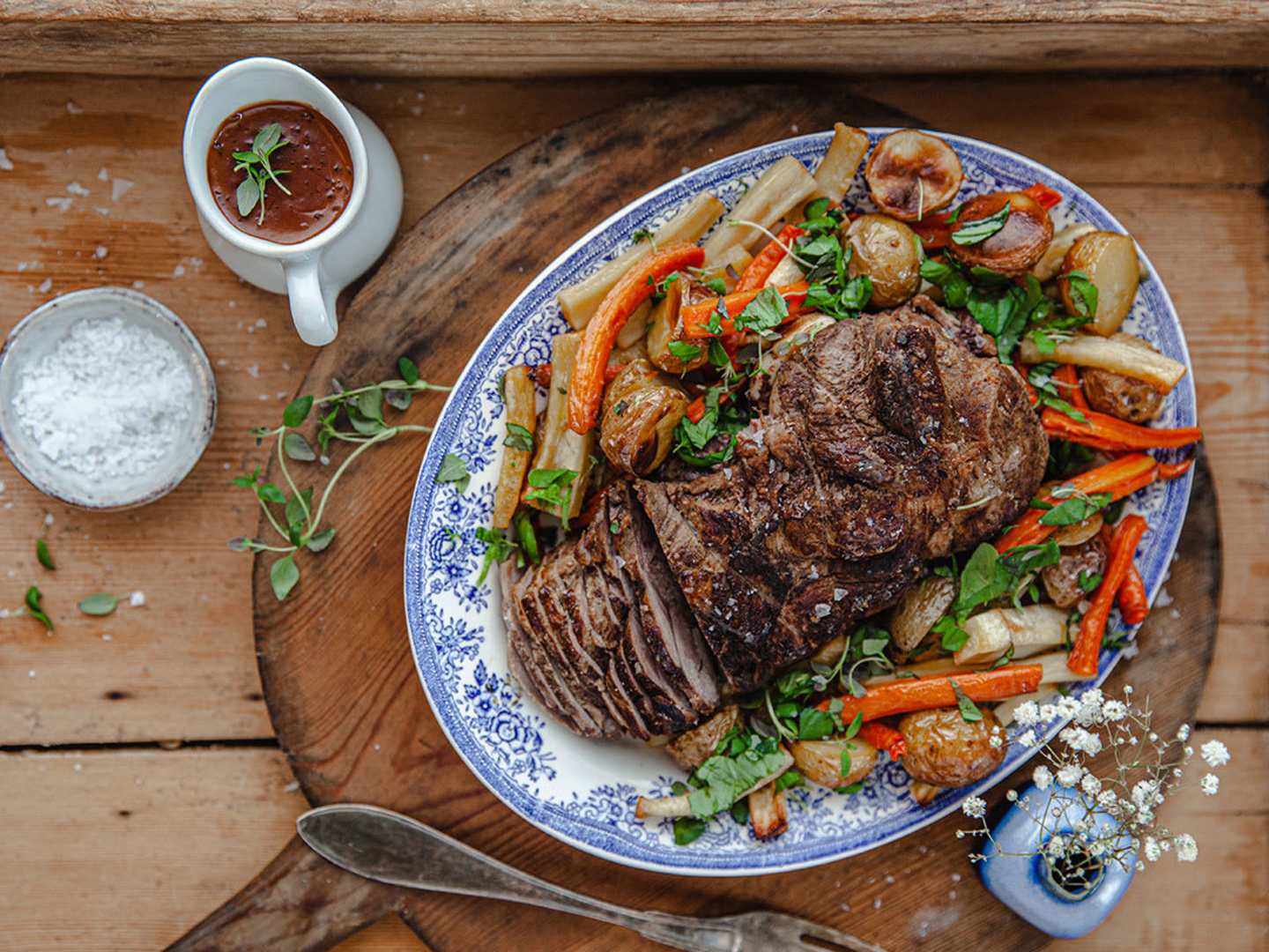Vildsvinsstek med rotsaker och örtig gräddsås, på vitblå tallrik på ett träbord.