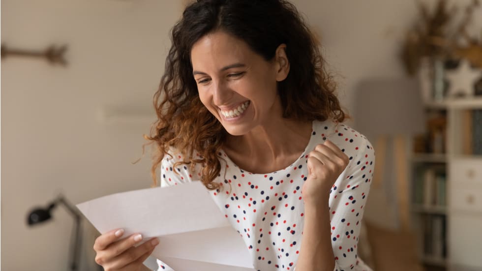Happy excited woman reading paper letter and getting unbelievable good news, making yes winner hand gesture, celebrating loan or statement approval, job achieve, promotion, success