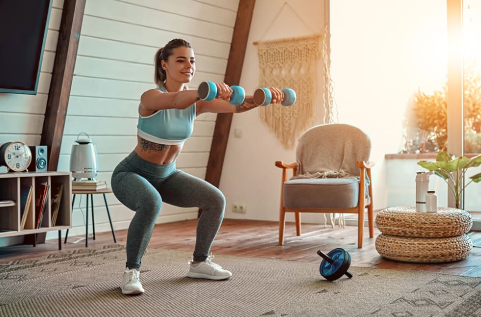 girl in leggings and top crouches with dumbbells at home. Sport, healthy lifestyle.