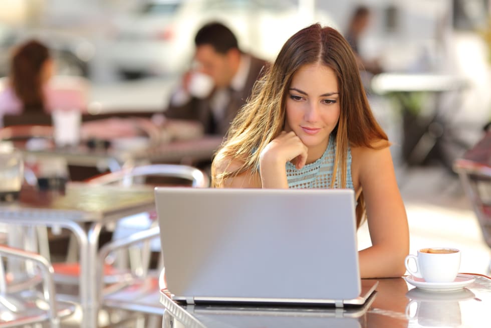 woman watching media in a laptop in a coffee shop with people in the background