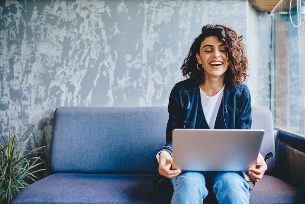 Happy stylish female blogger laughing while chatting with friends in social networks on laptop device using wireless internet in coworking