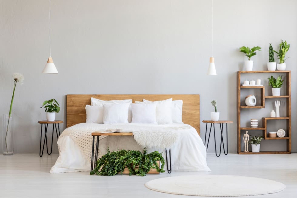 White pillows on wooden bed in minimal bedroom interior with plants and round rug.