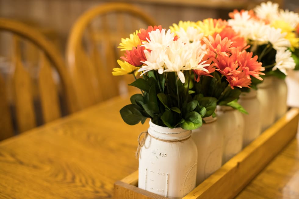 Arrangement of artificial spring flowers in painted canning jars on an oak table.