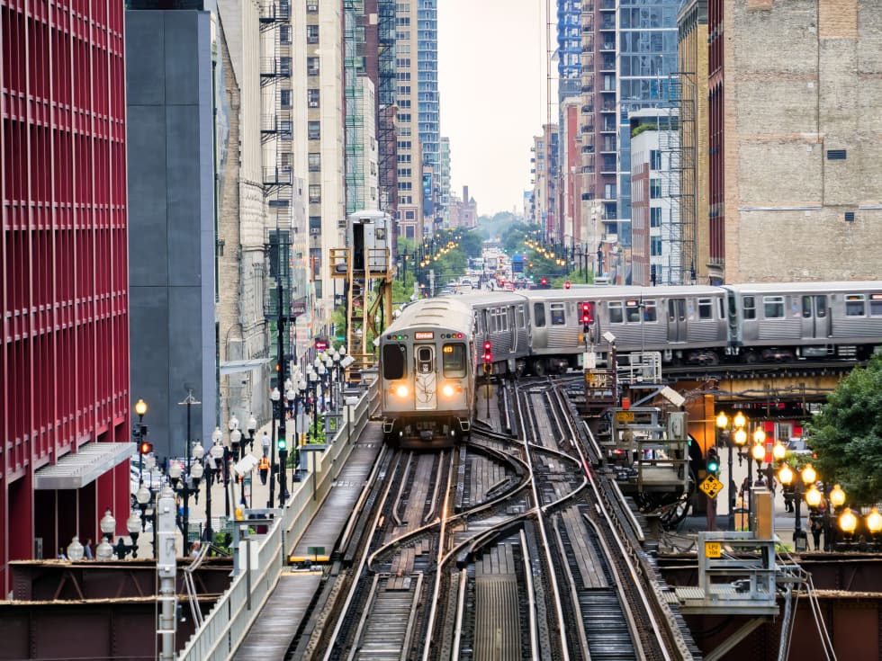 Train on elevated tracks within buildings at the Loop, Glass and Steel bridge between buildings - Chicago City Center - cost of living in chicago