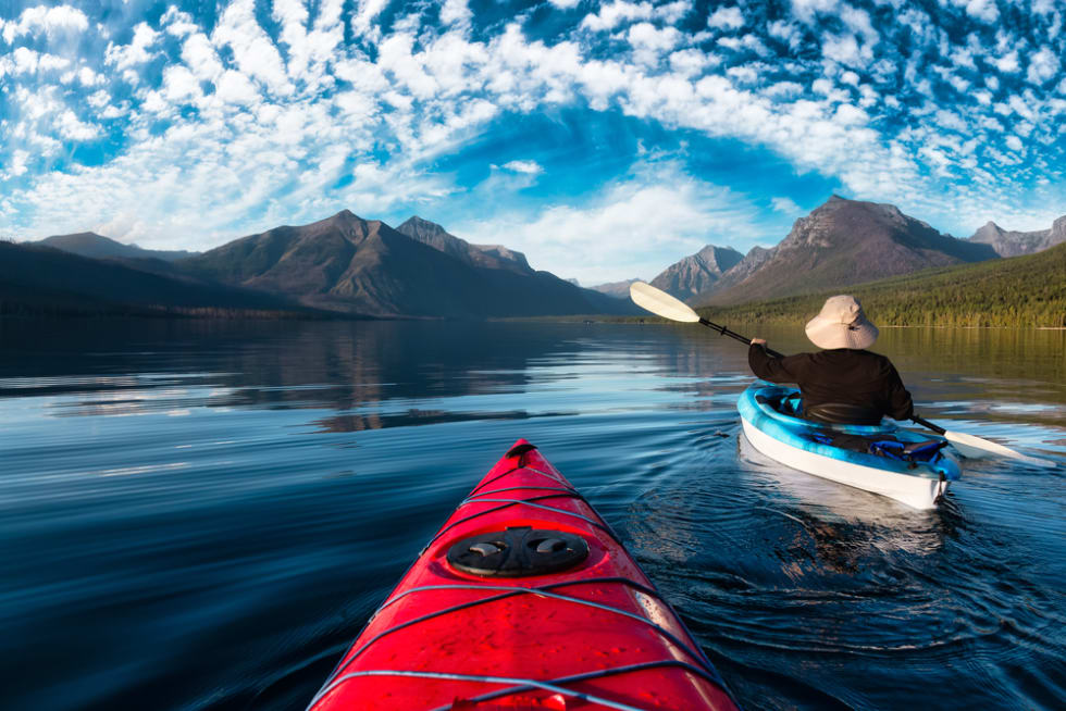 Adventurous Man Kayaking in Lake McDonald during a sunny summer evening with American Rocky Mountains in the background. Taken in Glacier National Park, Montana, USA.