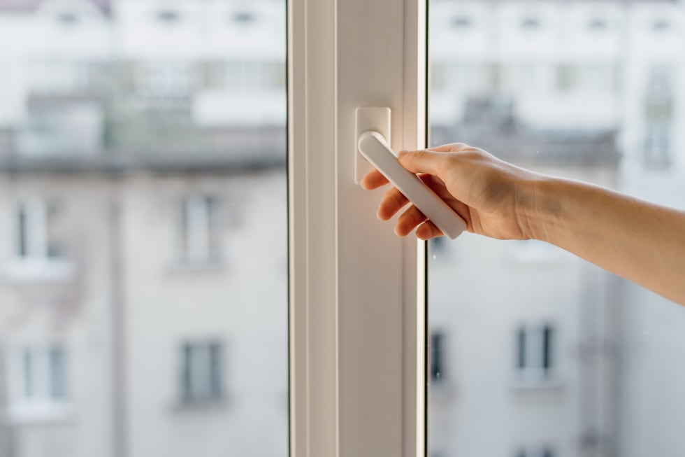 Cropped view of woman hand open pvc window with double glazing. Concept of noise cancellation and airing the room