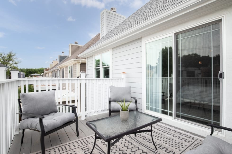 A home balcony with white spindles, composite decking, and outdoor furniture.