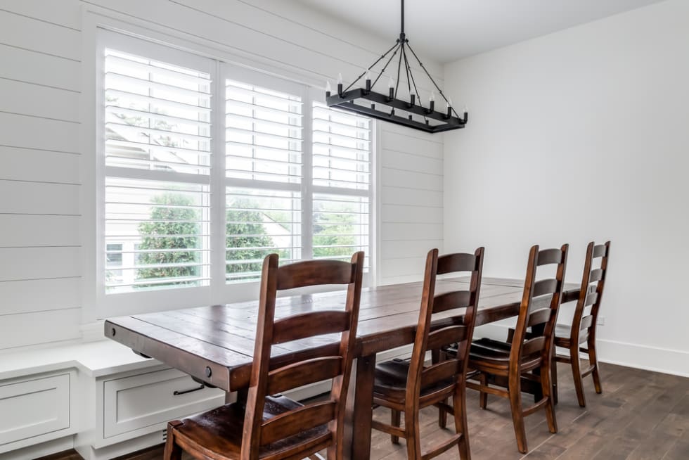 A modern farmhouse dining room with a shiplap wall, a large wooden table with chairs and bench seating, and a large black chandelier hanging from above.