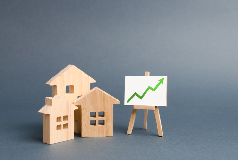 Wooden figures of houses and a poster with green arrow up. Increase liquidity and attractiveness of assets. Raising the rent or cost of buying a home.