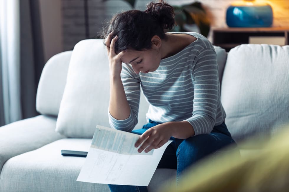 Shot of worried young woman thinking about her problems while holding bills of home - lease violation letter