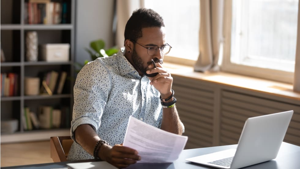 landlord holding documents looking at laptop computer screen