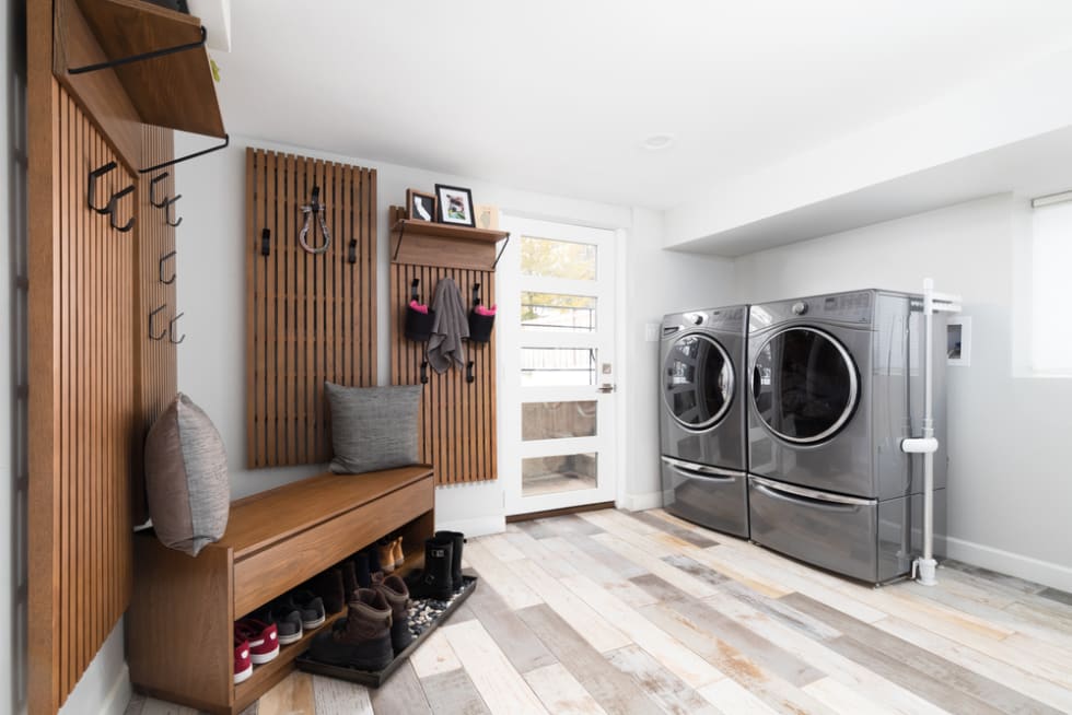 A renovated laundry room and mud room with Whirlpool washer and dryer, tile flooring, and coat hooks mounted on the wall.