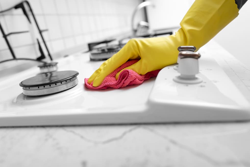 Hands in yellow gloves washing the gas stove.