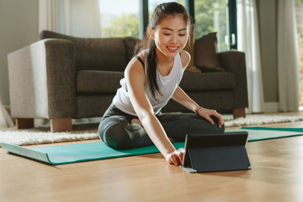 Smiling woman sitting exercise mat and watching training videos on digital tablet.