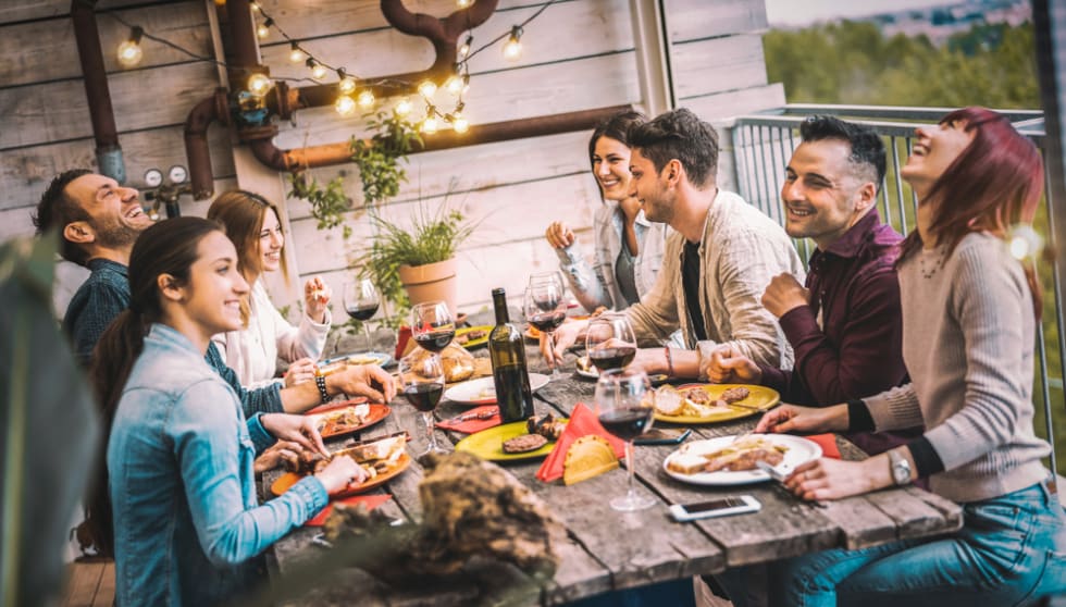 Young people dining and having fun drinking red wine together on balcony rooftop dinner party