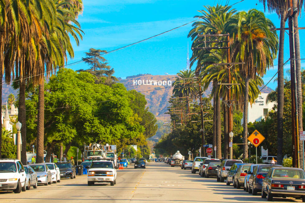 Hollywood sign district in Los Angeles, USA. Beautiful Hollywood highway road with cars, palms and a sign on the hills. Clear blue sky.