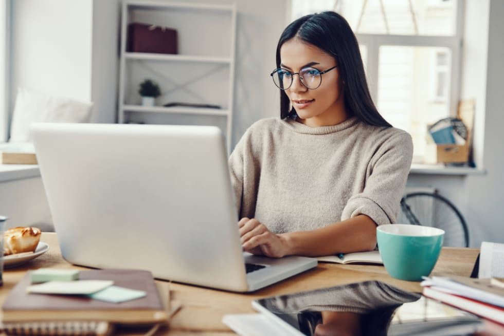 Woman in casual clothing using laptop and smiling while working indoors