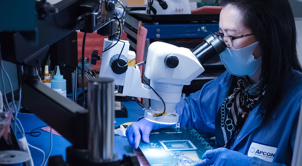 A woman looking at a motherboard with a microscrope.