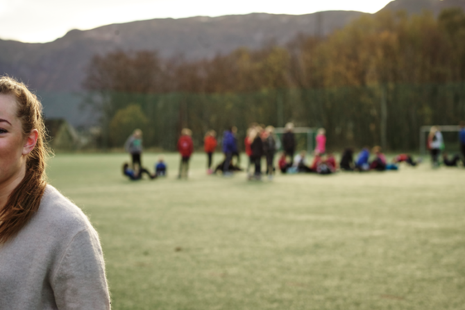Jente på fotball banen med mange ungdommer