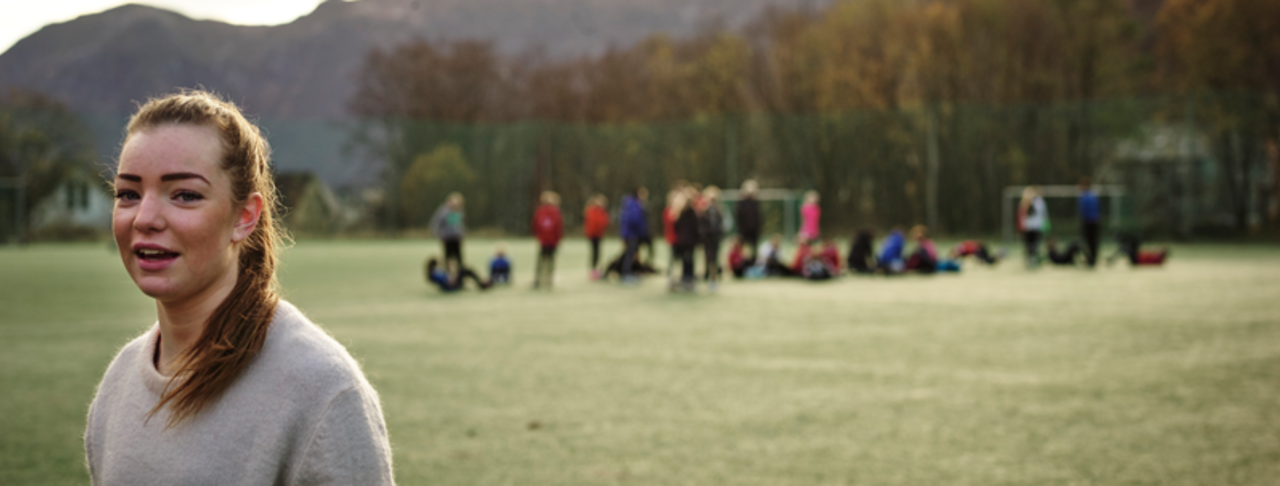 Jente på fotball banen med mange ungdommer