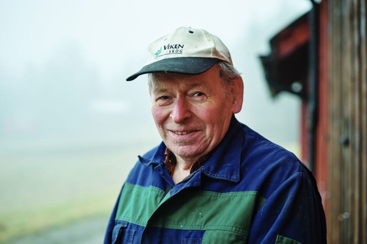 En eldre bondekar står foran det som ser ut som en hytte, landskapet bak ligger i tåke. Foto: Øivind Haug