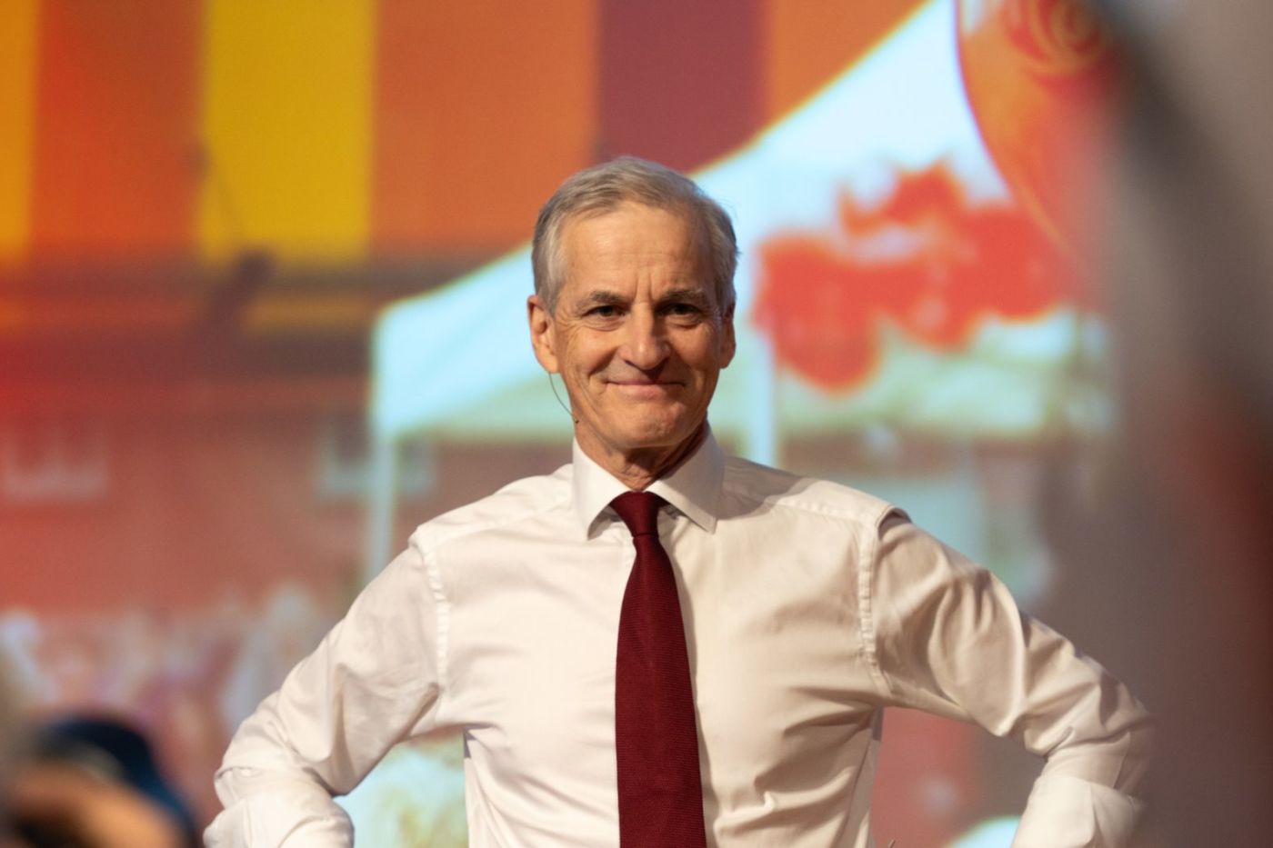 Statsminister Jonas Gahr Støre i hvit skjorte og med mørkerødt slips står på en scene.