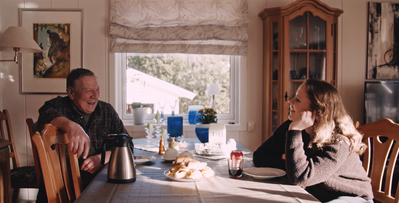 Ung jente og eldre mann sitter ved bord og prater.