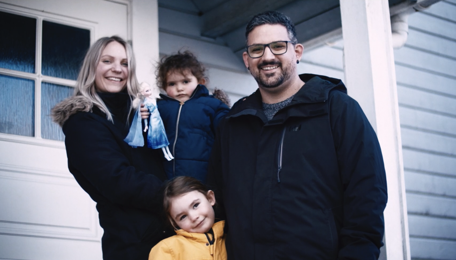 Familie på fire som står utenfor et hus. To barn, mann og kvinne.