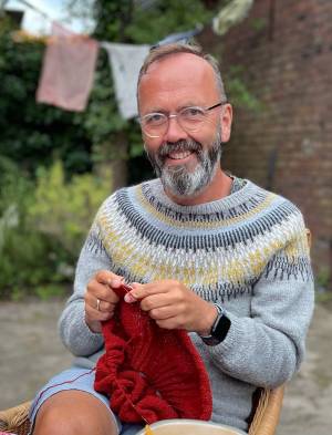 Stein helge sitt i hagen og strikkar, medan han smilar til kamera