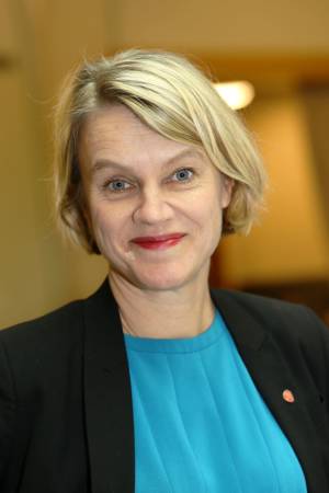 Kvinne som smiler, med lå topp og sort jakke.