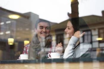 Bilde av et ungt par på café, bildet er tatt fra andre siden av et vindu. Foto: Øivind Haug