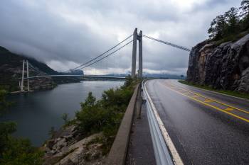 I forgrunnen ser vi en vei langs en fjord, og i bakgrunnen en flott bru over fjorden.