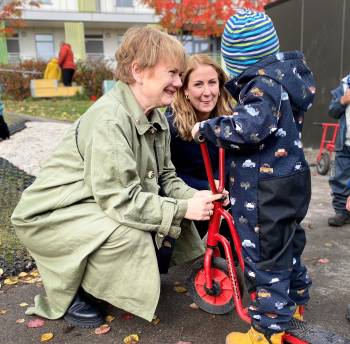 Ragnhild Bergheim og Tonje Brenna sitter på huk og snakker med barn på sparkesykkel